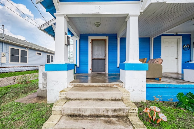 view of exterior entry with fence and covered porch