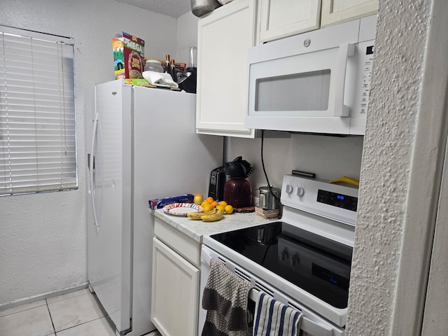 kitchen featuring light countertops, light tile patterned floors, a textured wall, white cabinets, and white appliances