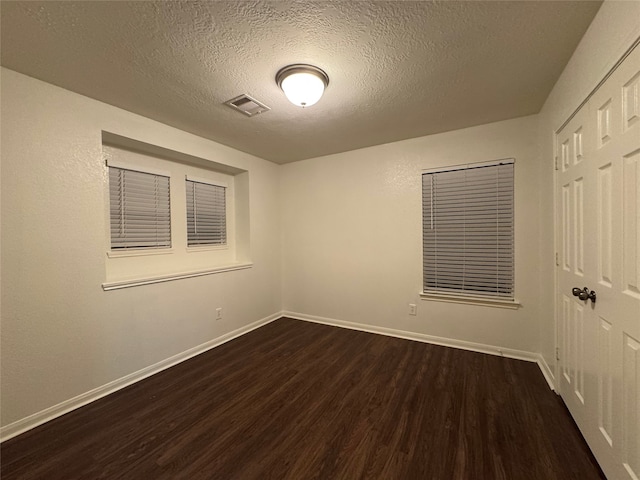 unfurnished bedroom with dark wood-style floors, visible vents, a textured ceiling, and baseboards