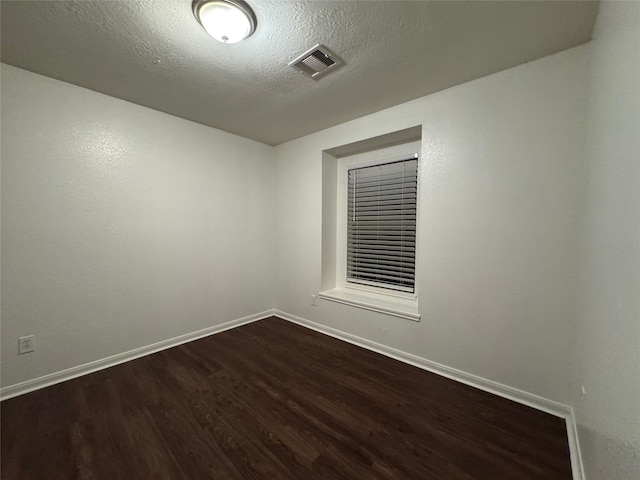 spare room with dark wood finished floors, visible vents, a textured ceiling, and baseboards