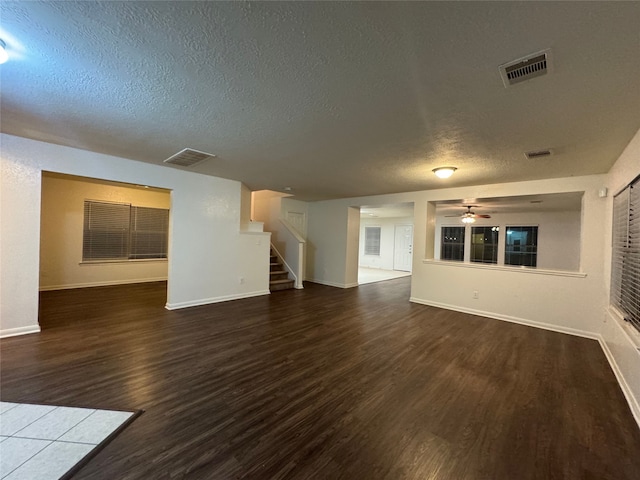 unfurnished living room featuring visible vents, stairway, a textured ceiling, and wood finished floors