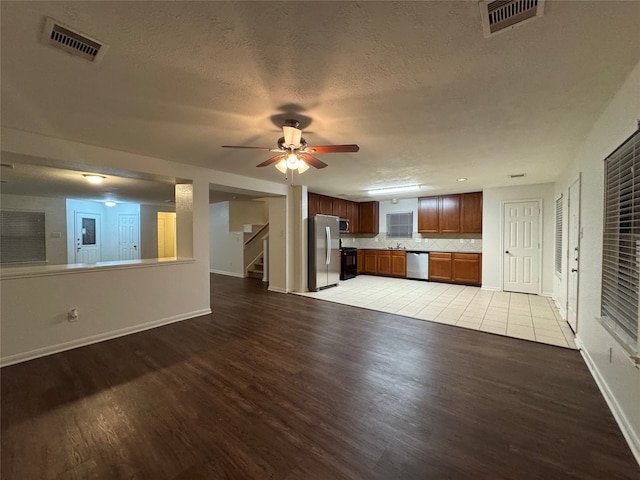 unfurnished living room featuring visible vents, stairway, a textured ceiling, and wood finished floors