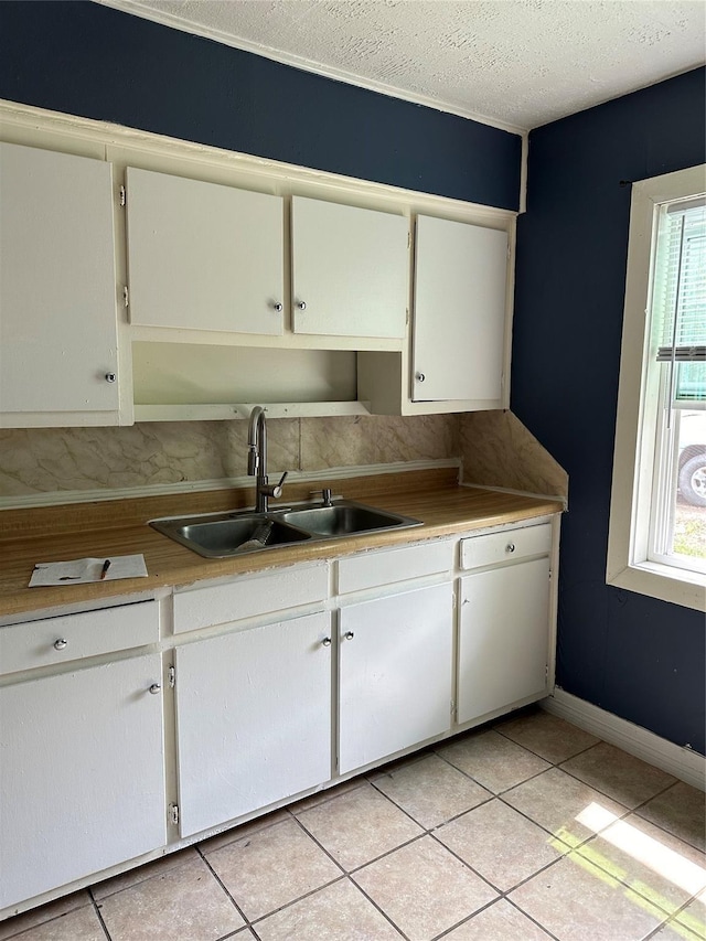 kitchen featuring baseboards, a sink, light countertops, white cabinets, and a textured ceiling