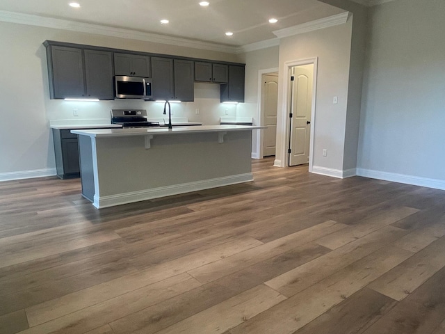 kitchen with dark wood finished floors, stainless steel appliances, crown molding, and a kitchen island with sink