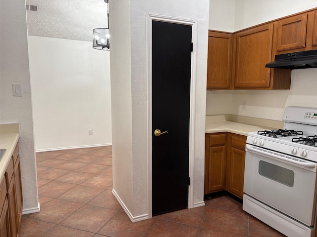 kitchen featuring visible vents, white gas range, under cabinet range hood, and brown cabinets