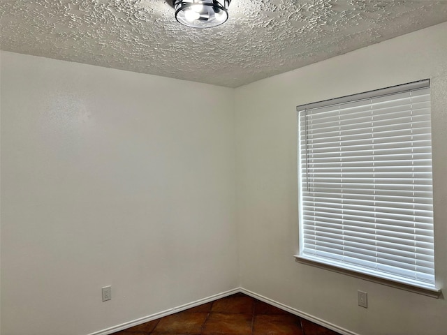 empty room featuring dark tile patterned floors, baseboards, and a textured ceiling