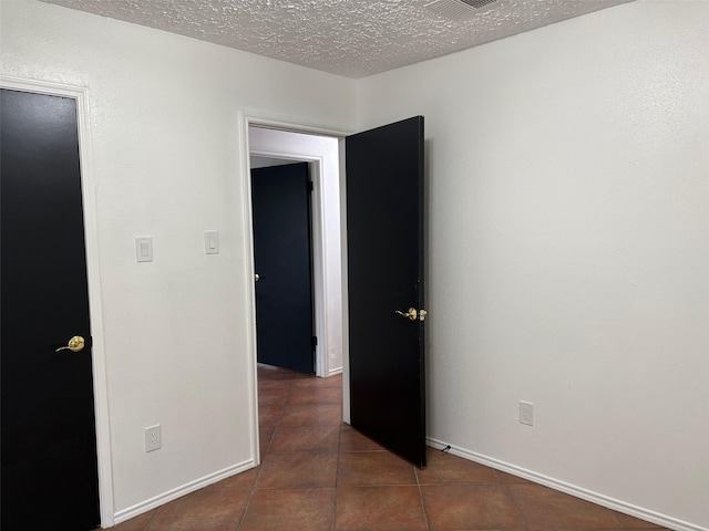 tiled empty room featuring a textured ceiling and baseboards