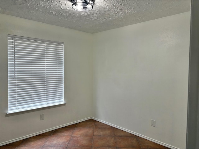 empty room with baseboards, a textured ceiling, and tile patterned flooring