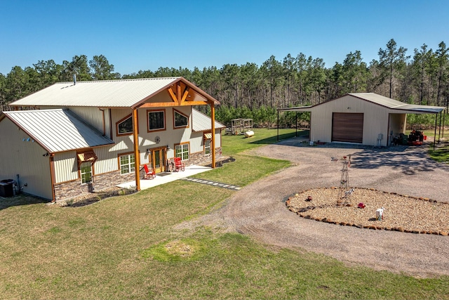 exterior space featuring aphalt driveway, stone siding, a detached garage, a yard, and metal roof