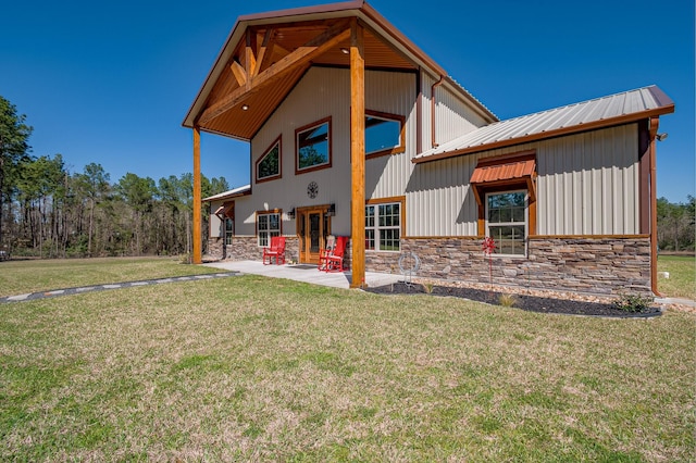 rear view of house featuring a yard, stone siding, and a patio