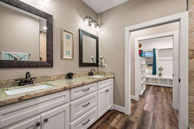 full bath with double vanity, wood finished floors, baseboards, and a sink