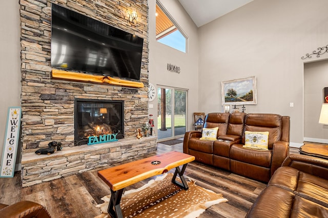 living area featuring a stone fireplace, a high ceiling, baseboards, and wood finished floors