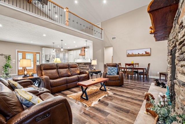 living area with wood finished floors, visible vents, baseboards, recessed lighting, and a towering ceiling