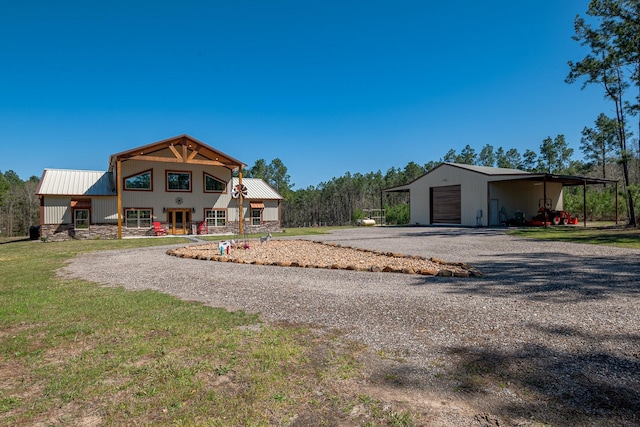 back of house with metal roof, a detached garage, gravel driveway, and an outdoor structure