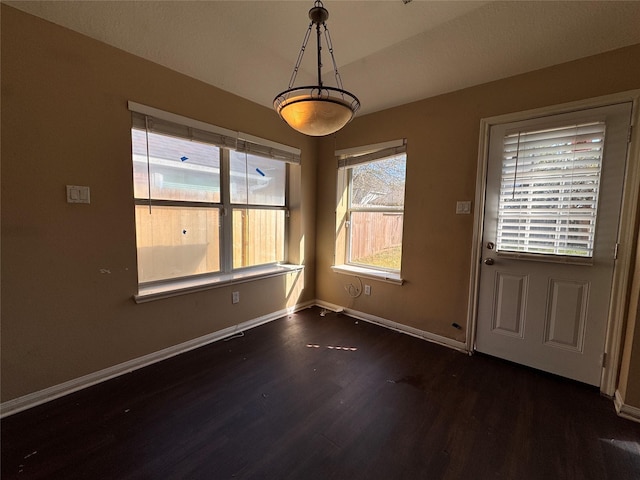 unfurnished dining area featuring baseboards and dark wood-style floors