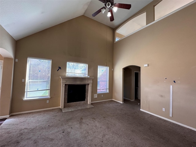 unfurnished living room with a fireplace with flush hearth, arched walkways, carpet, baseboards, and ceiling fan