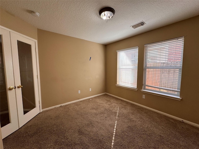 carpeted spare room with visible vents, baseboards, a textured ceiling, and french doors