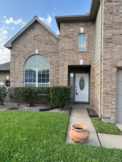 doorway to property featuring brick siding and a lawn