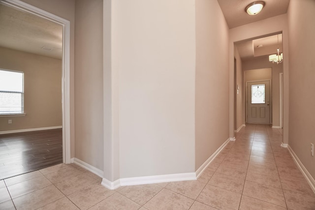 corridor featuring light tile patterned floors, baseboards, and a notable chandelier