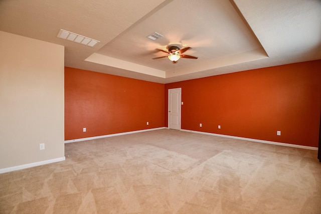 unfurnished room with a raised ceiling, baseboards, visible vents, and ceiling fan