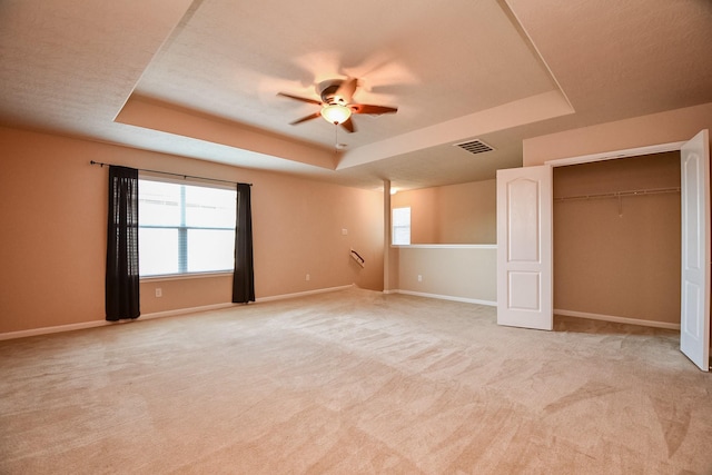 unfurnished bedroom featuring visible vents, light carpet, multiple windows, a tray ceiling, and baseboards