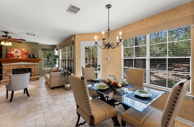 dining area featuring a stone fireplace, stone finish floor, ceiling fan with notable chandelier, and visible vents