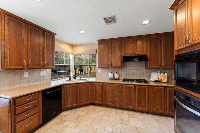 kitchen featuring visible vents, under cabinet range hood, brown cabinetry, black appliances, and a sink