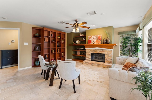 living area with a stone fireplace, baseboards, visible vents, and a ceiling fan