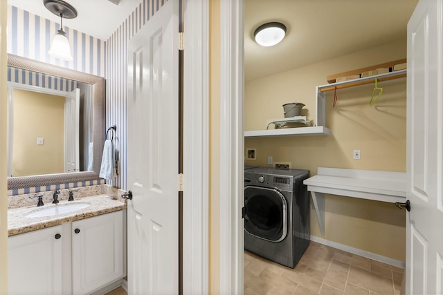 washroom with a sink, wallpapered walls, baseboards, washer / dryer, and laundry area