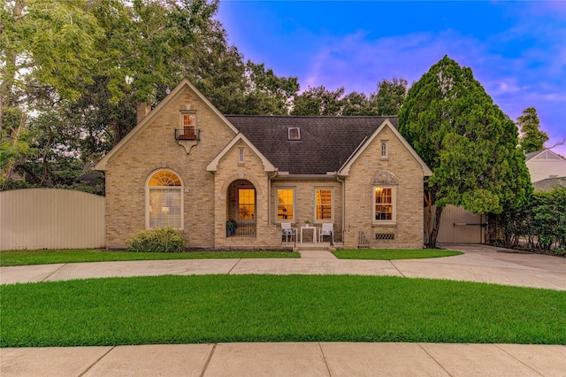 view of front of house featuring brick siding, roof with shingles, a front yard, and fence