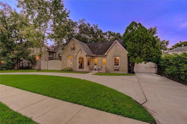 view of front facade featuring brick siding, concrete driveway, a front lawn, and a gate