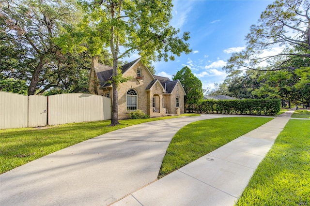 french country inspired facade with stone siding, fence, a front lawn, and a gate