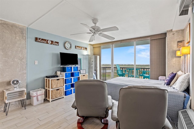 bedroom with a ceiling fan, wood finished floors, visible vents, expansive windows, and access to outside