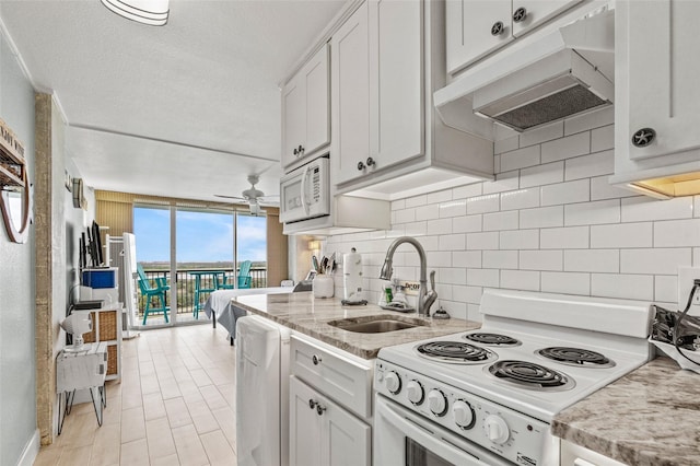 kitchen with white appliances, a sink, under cabinet range hood, expansive windows, and backsplash