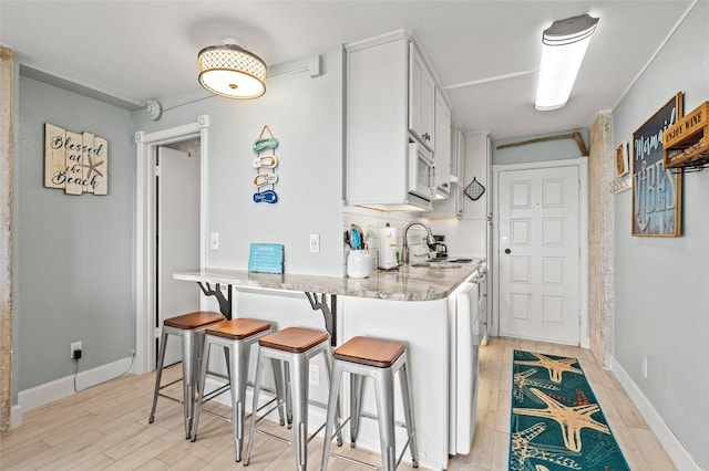 kitchen featuring white microwave, white cabinets, a kitchen breakfast bar, and light wood-type flooring