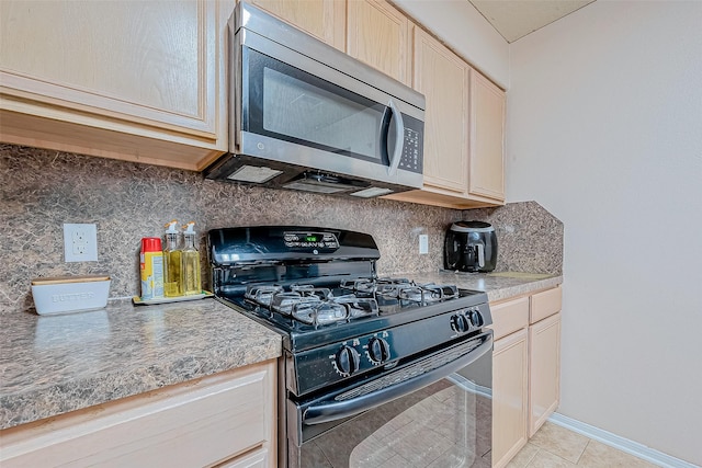 kitchen featuring black gas range, stainless steel microwave, light tile patterned floors, decorative backsplash, and baseboards