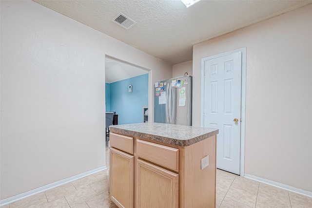 kitchen featuring visible vents, light tile patterned flooring, freestanding refrigerator, light brown cabinetry, and a center island