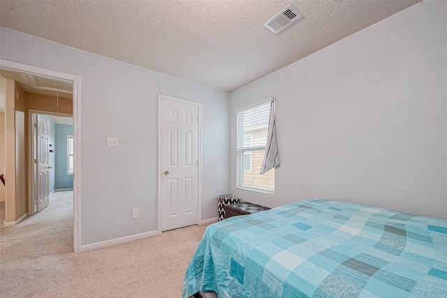 bedroom with visible vents, baseboards, light colored carpet, attic access, and a textured ceiling