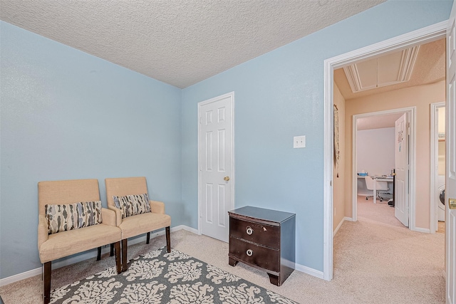 sitting room featuring light colored carpet, baseboards, a textured ceiling, and attic access