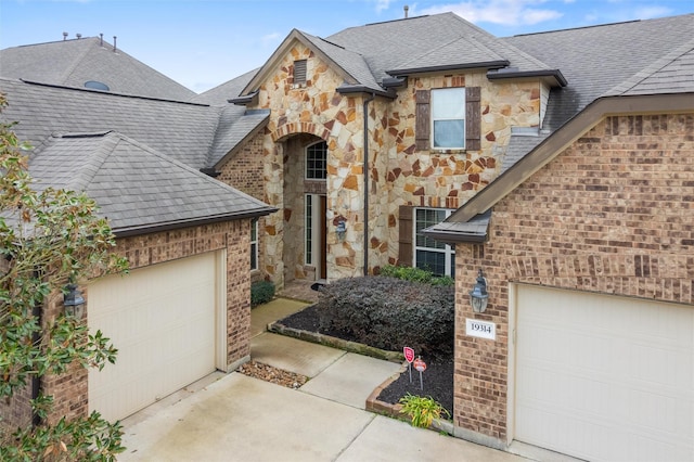 view of front of property with roof with shingles, concrete driveway, stone siding, a garage, and brick siding