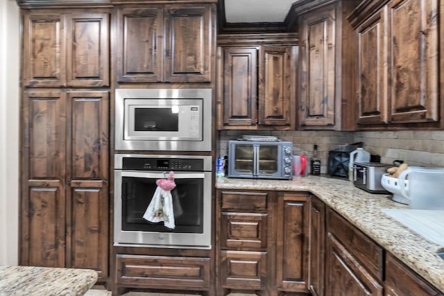 kitchen with dark brown cabinetry, light stone counters, and appliances with stainless steel finishes