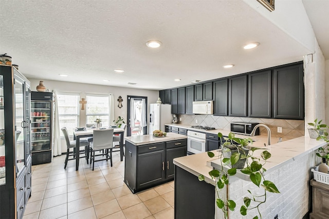 kitchen with wine cooler, white appliances, light tile patterned flooring, light countertops, and decorative backsplash