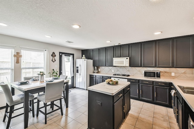 kitchen with white appliances, light tile patterned floors, visible vents, decorative backsplash, and a center island