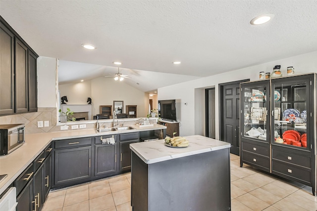 kitchen featuring a peninsula, light tile patterned flooring, a sink, stainless steel microwave, and open floor plan