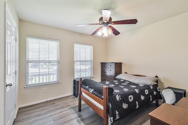 bedroom featuring multiple windows, ceiling fan, baseboards, and wood finished floors