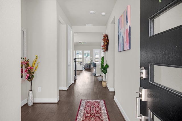 hall with visible vents, baseboards, and dark wood-style flooring