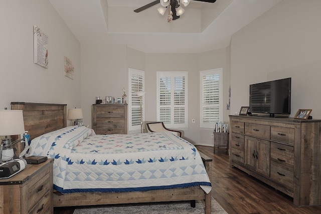 bedroom featuring a raised ceiling, dark wood-type flooring, and ceiling fan