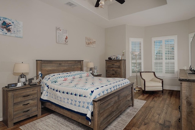 bedroom with visible vents, ceiling fan, baseboards, a tray ceiling, and dark wood-style flooring