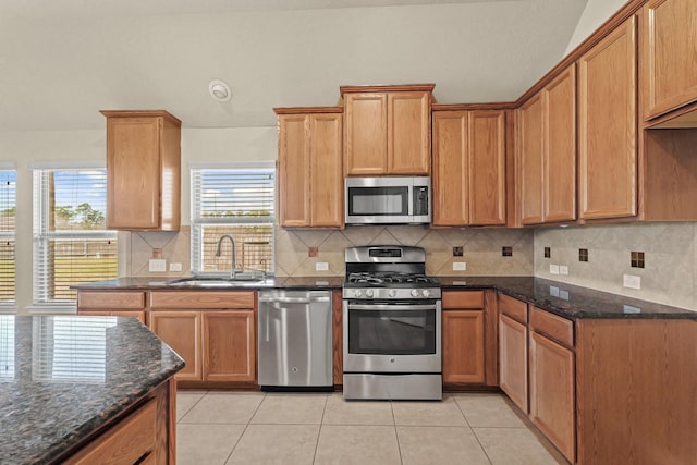 kitchen with light tile patterned floors, appliances with stainless steel finishes, dark stone counters, and a sink