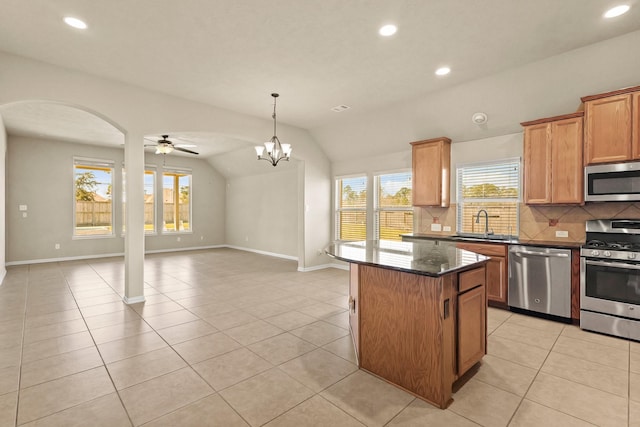 kitchen with backsplash, a kitchen island, appliances with stainless steel finishes, light tile patterned floors, and vaulted ceiling